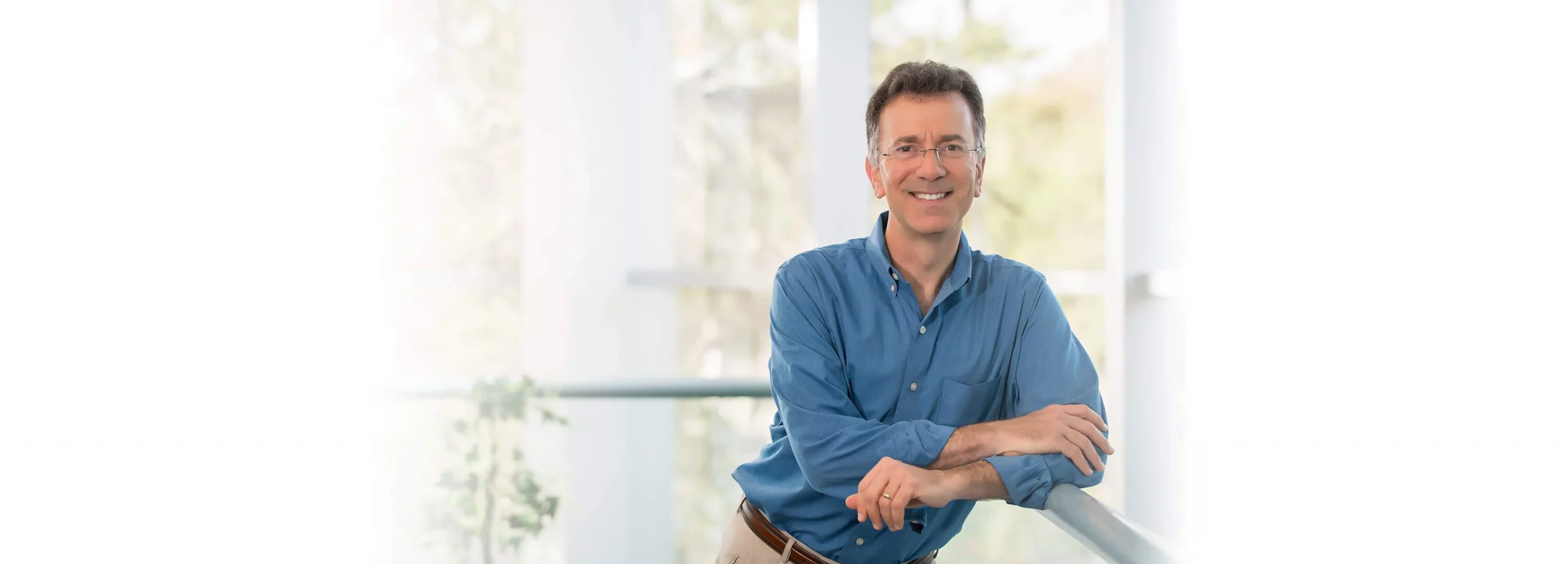 Dr. David Rosenberg standing in the practice, arms folded, bright window light behind him.